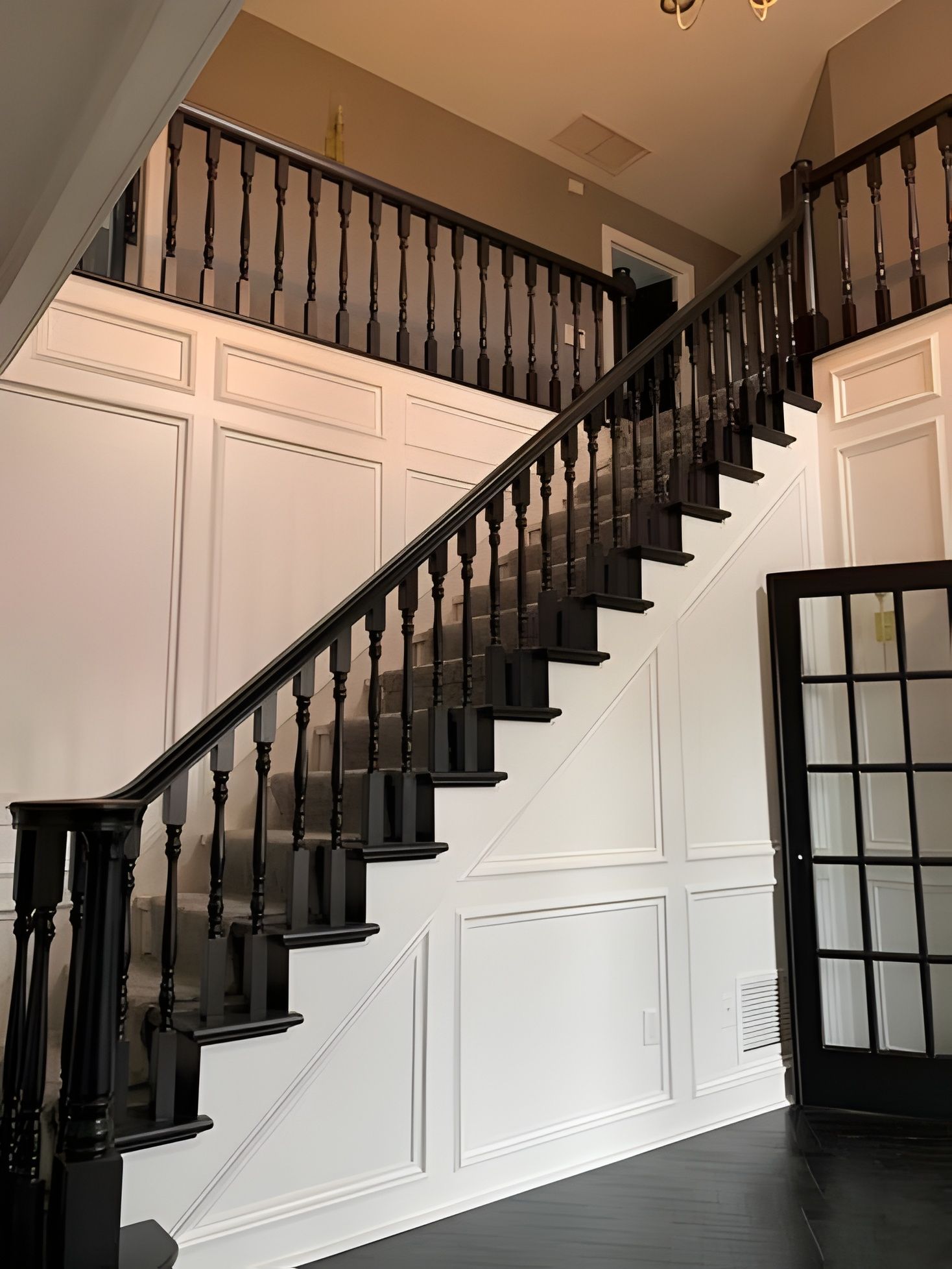 Grand foyer featuring a staircase with black wooden railings and white paneled walls leading to an upstairs balcony.