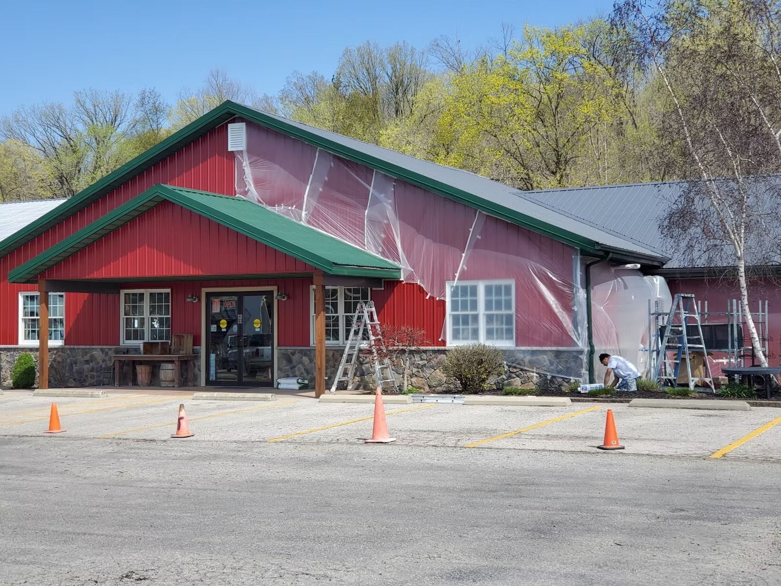 A red commercial building with a green roof is under construction, covered in plastic sheeting with a ladder outside.
