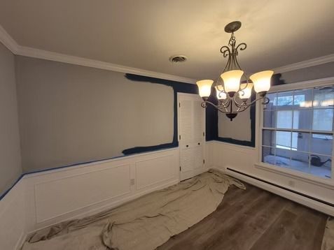 A room interior with white wainscoting and a partly painted dark blue wall, featuring a chandelier and wood floors.