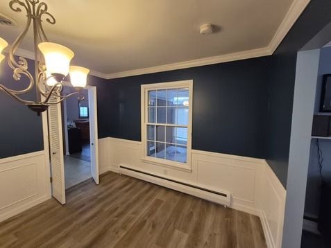 A dining room with navy blue upper walls, white wainscoting, a chandelier, and a window overlooking a sunroom.