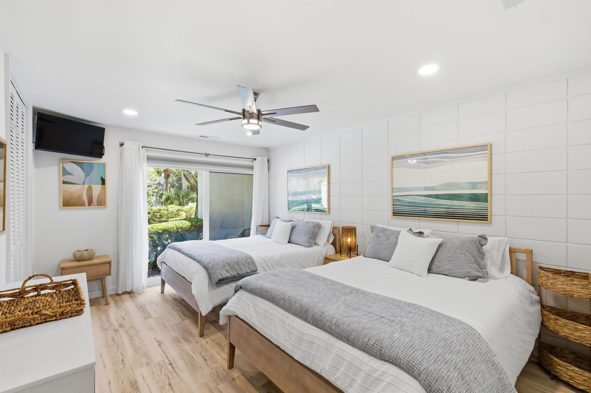 A cozy, neatly made bed with a white comforter and beige knit throw, next to a window with a plant and natural sunlight.