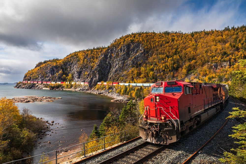 A man is kneeling down next to a train and looking at it.