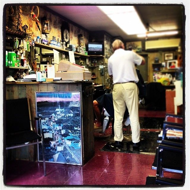 Man standing in a cluttered shop or bar, facing a counter under warm fluorescent lights.