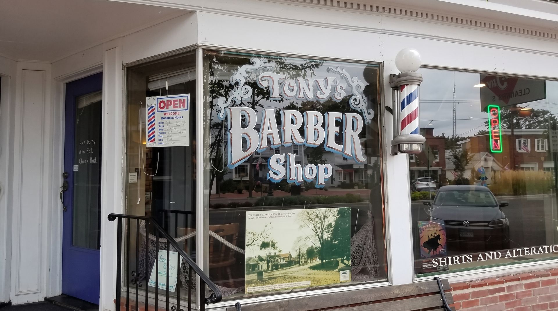 Barber shop storefront with glass windows, white awning, and red-white-blue barber pole on the right