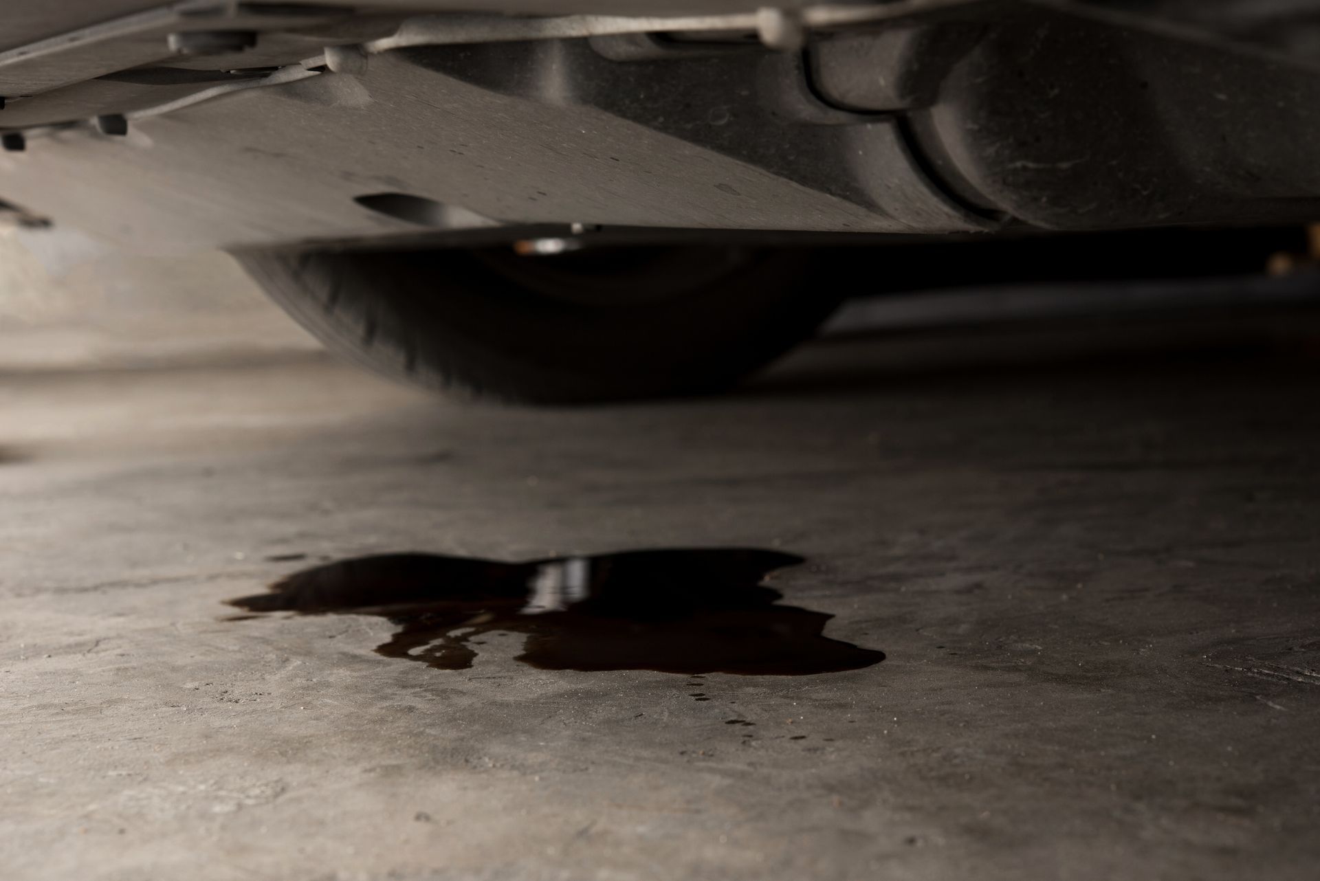 A puddle of oil is on the ground under a car.