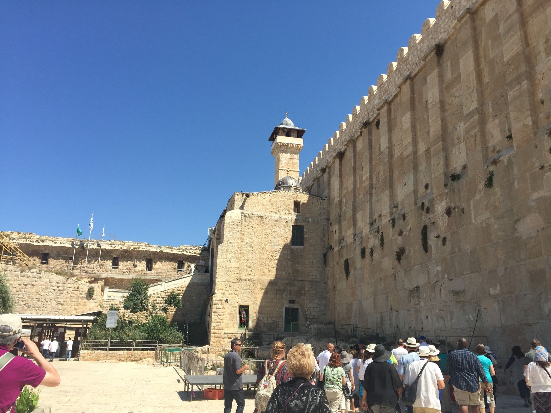 Tourists walking beside a massive stone wall at the Western Wall in bright daylight