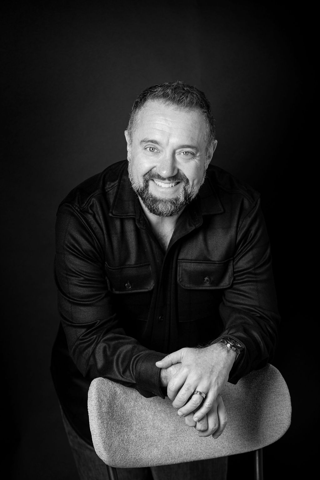 Smiling man leaning forward on a chair against a dark studio background