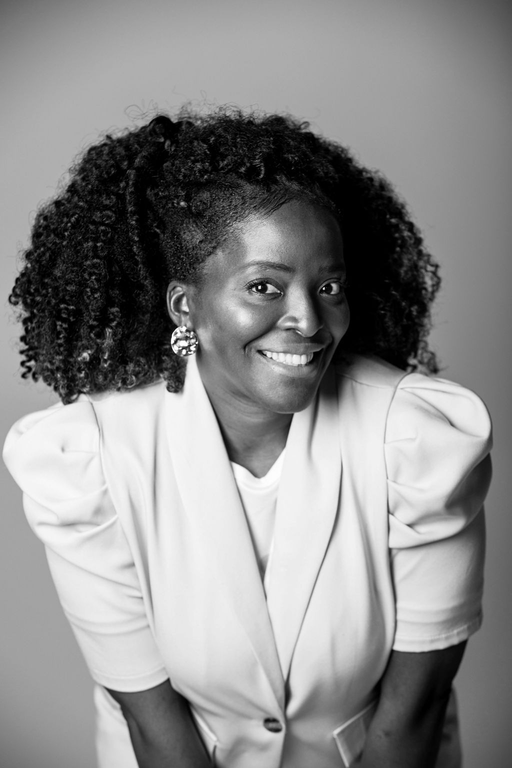 Smiling woman in a white blazer against a gray backdrop