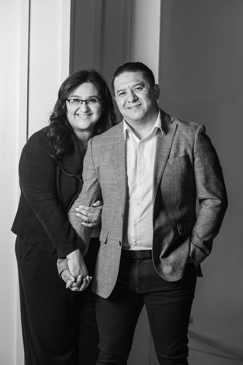 Two people standing together and smiling in a black-and-white portrait against a studio backdrop