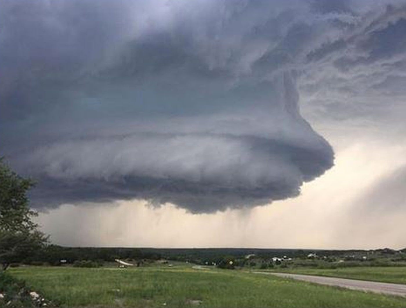 Massive dark storm cloud over a green field and road in a rural landscape