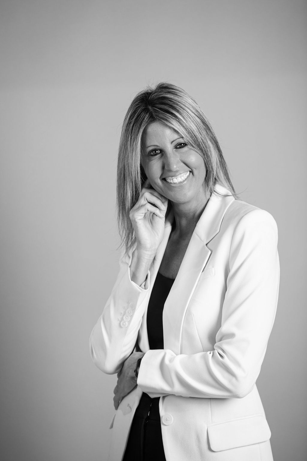 Smiling woman in a white blazer standing against a plain gray background