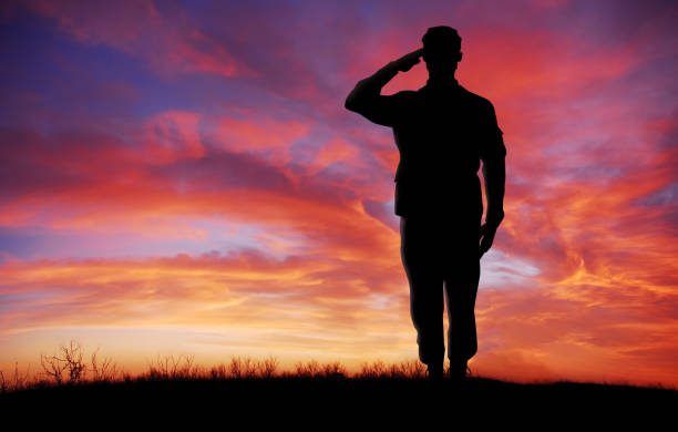 Silhouetted person salutes on a hill against a vivid pink and orange sunset sky