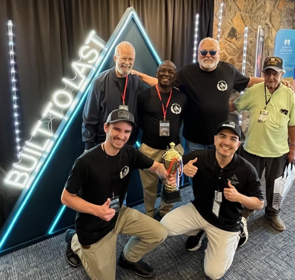 Group of five people posing at a conference booth with a glowing triangular 