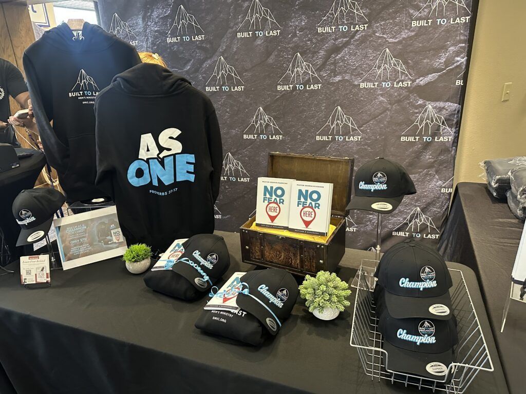 Black “AS ONE” hoodie and branded caps displayed on a table with small signs and flowers