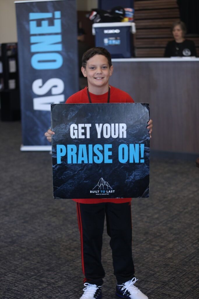 Person holding a sign that reads “GET YOUR PRAISE ON!” in a lobby area