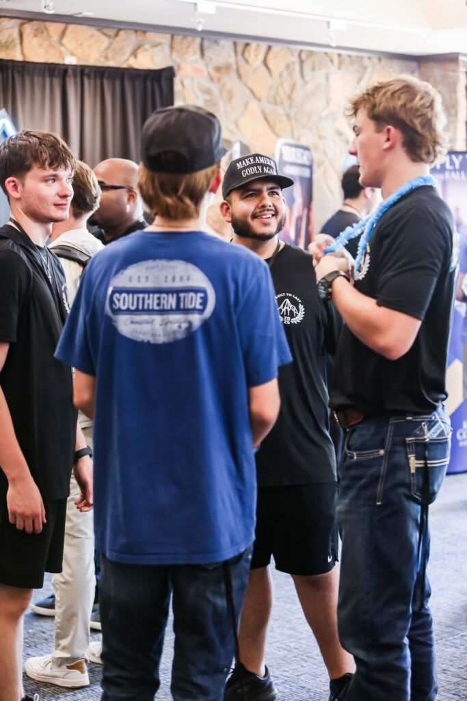 People chatting at an indoor event, with a man in a blue “SOUTHEIDE” shirt in the foreground