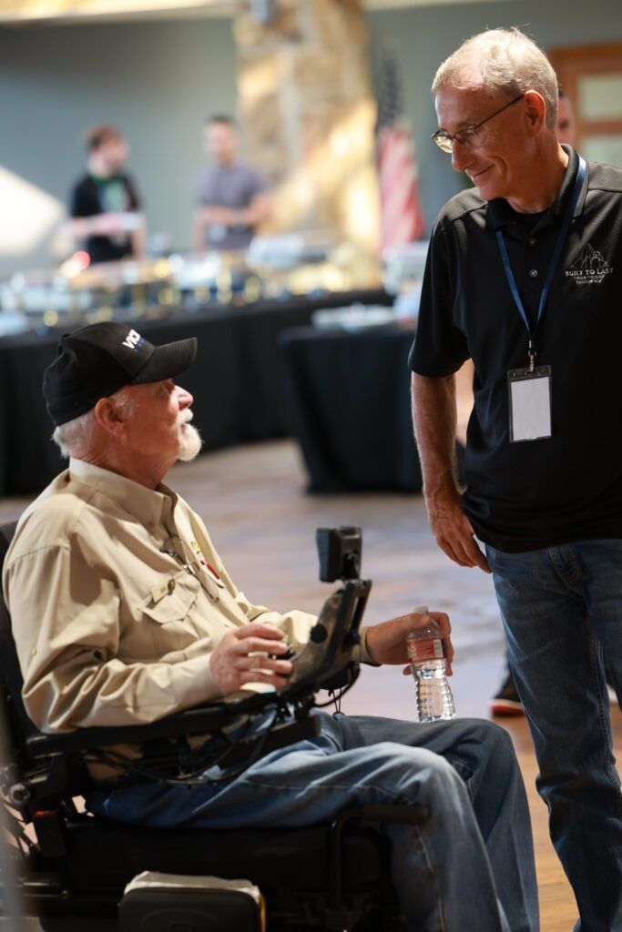 Two men talking at a conference, one seated in a wheelchair and one standing nearby.