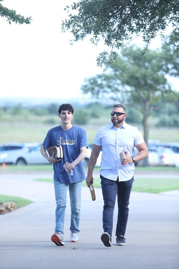 Two people walking on a tree-lined path, each holding a drink and a bag.