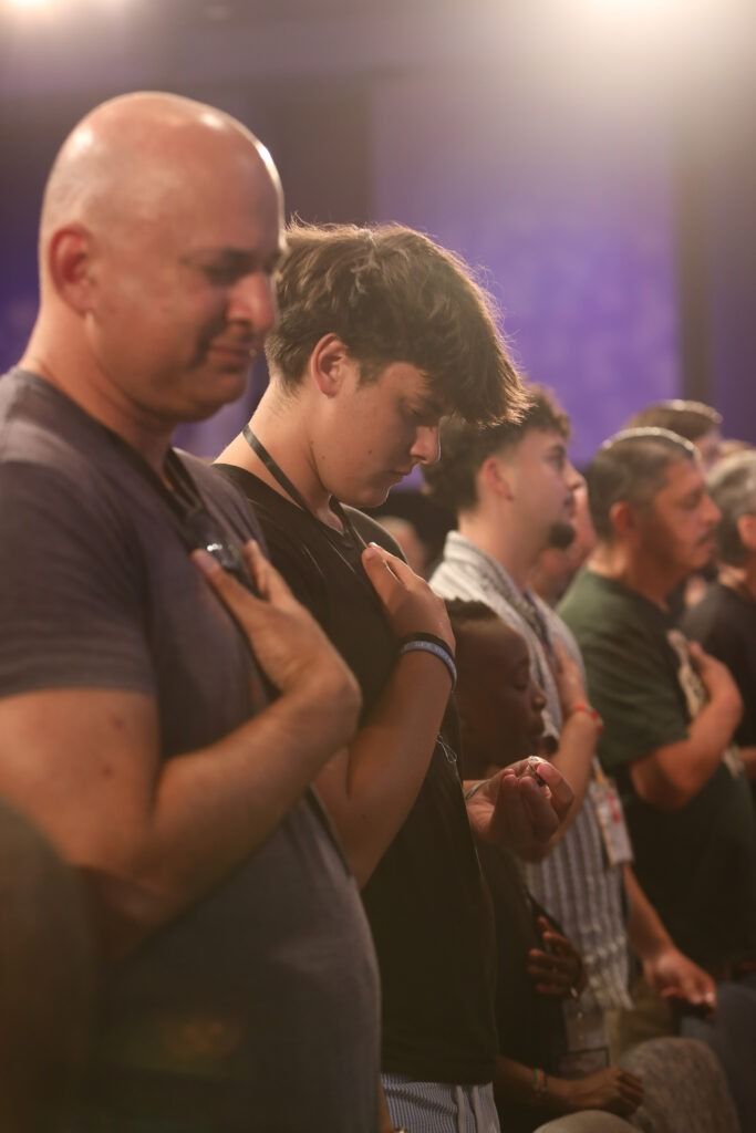 People standing with hands over hearts in a dimly lit indoor gathering
