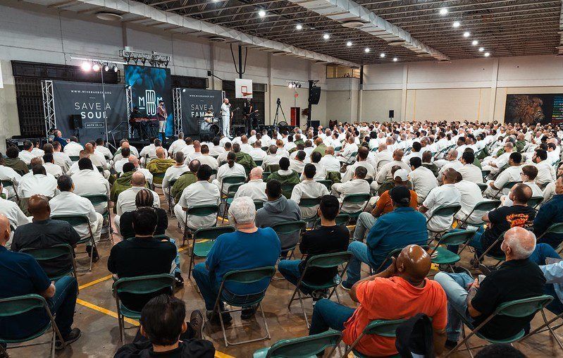 Large indoor audience seated in rows facing a stage at a convention or conference.