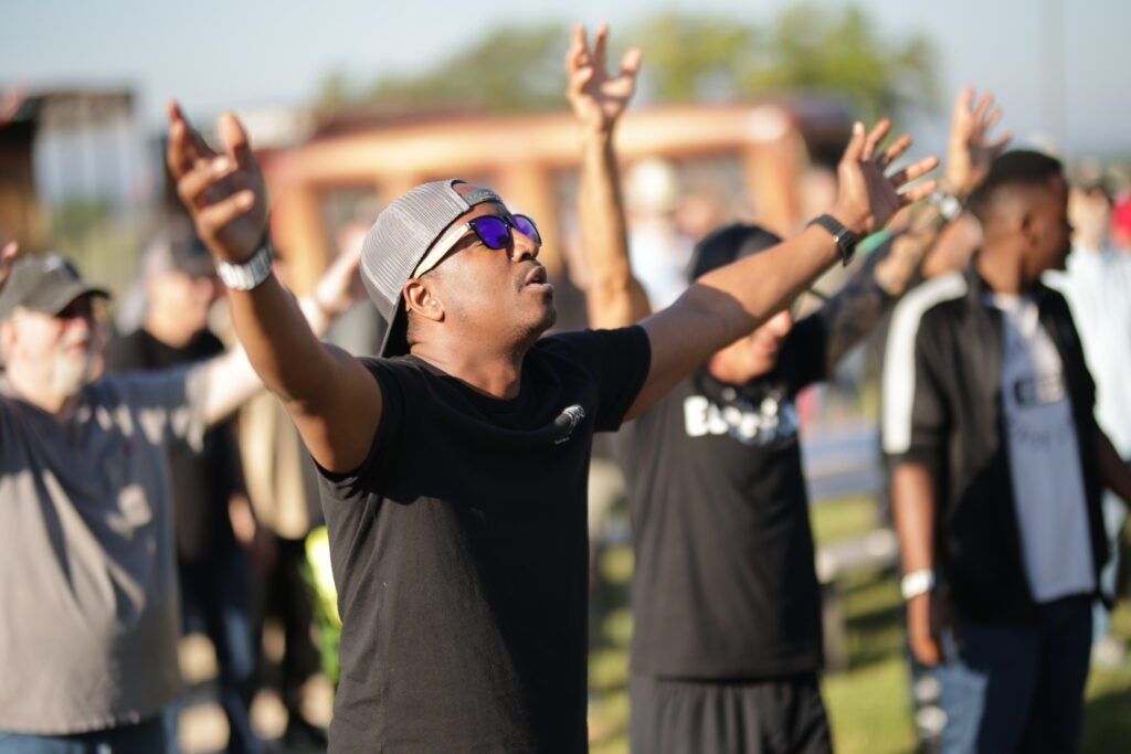 People with raised arms outdoors, wearing black shirts and sunglasses during a group gathering
