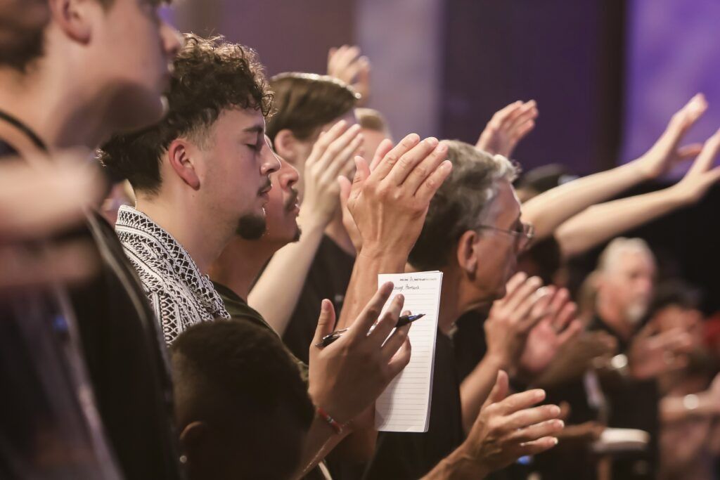 People standing and clapping in a crowded indoor gathering, hands raised in applause.