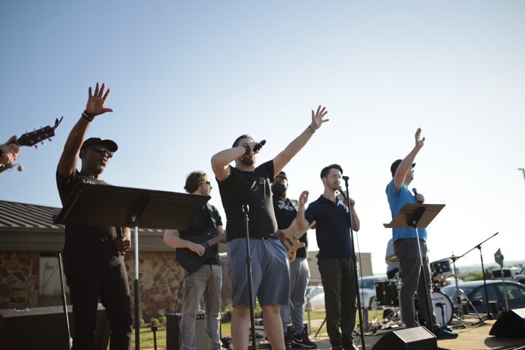 Musicians on an outdoor stage, some raising their hands during a live performance.