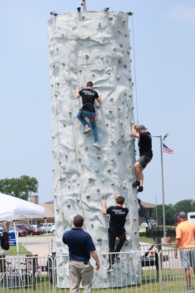 People climbing a tall white rock wall at an outdoor event