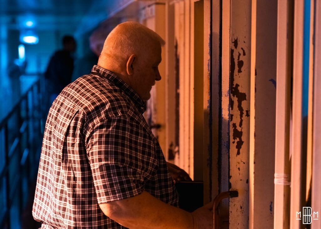 Person in a plaid shirt opening a door in a dimly lit hallway with blue and orange lighting