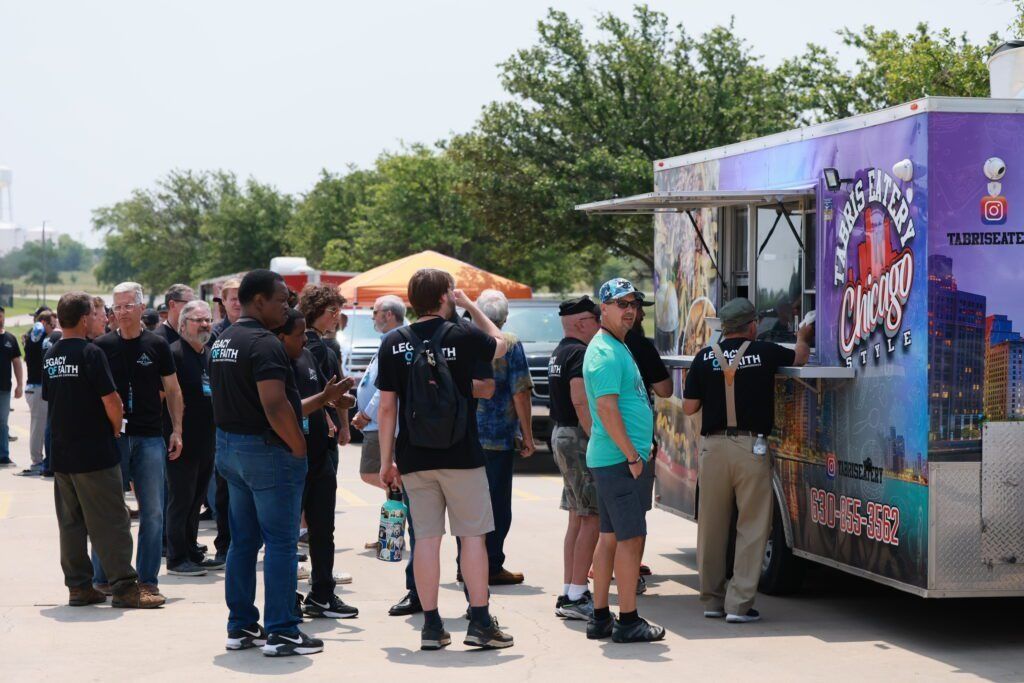 People standing in line at an outdoor food truck on a sunny day