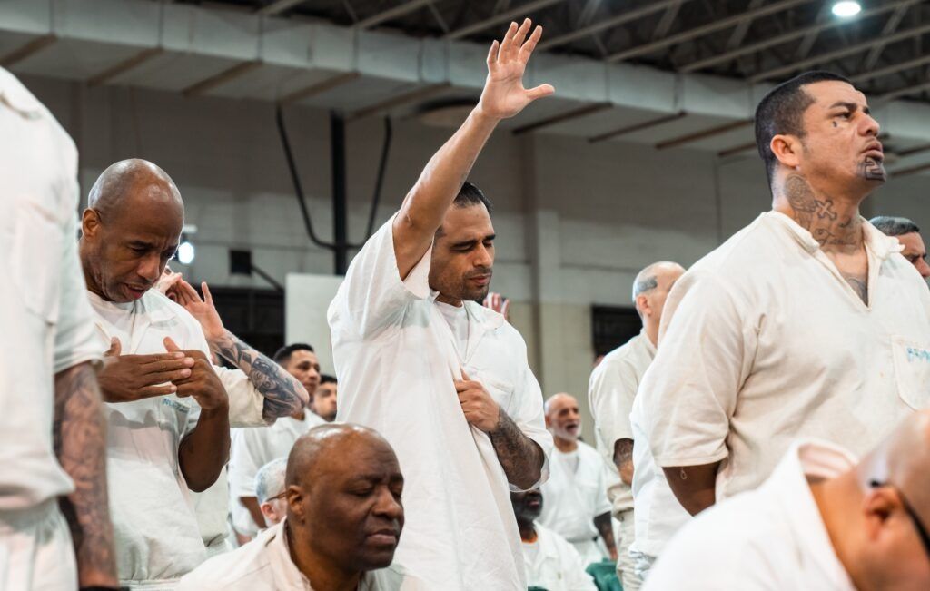 People in white clothing standing and raising hands in a crowded indoor setting