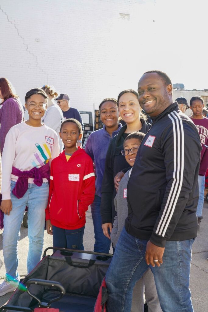 Group of smiling people posing outdoors, with a man in a black tracksuit in the foreground.