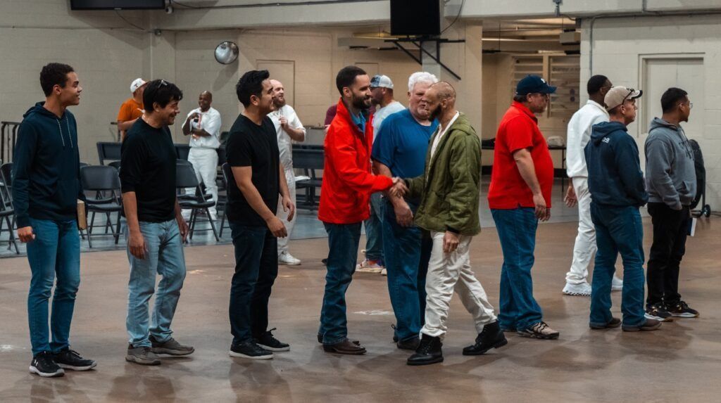 People standing in a line on a gym floor, some in red and blue jackets, in a large indoor hall