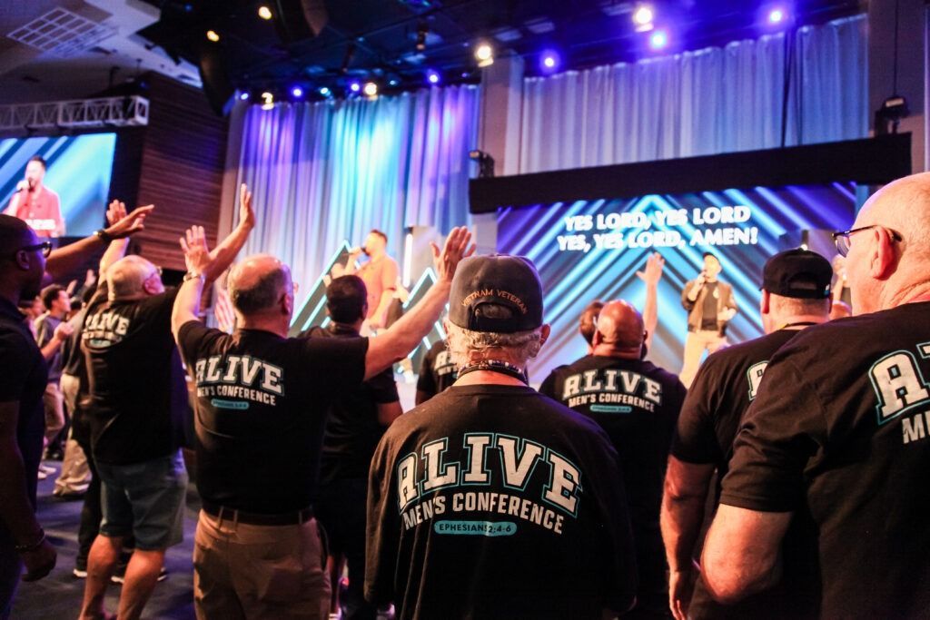 Crowd with raised hands at a LIVE conference stage with blue-purple lighting