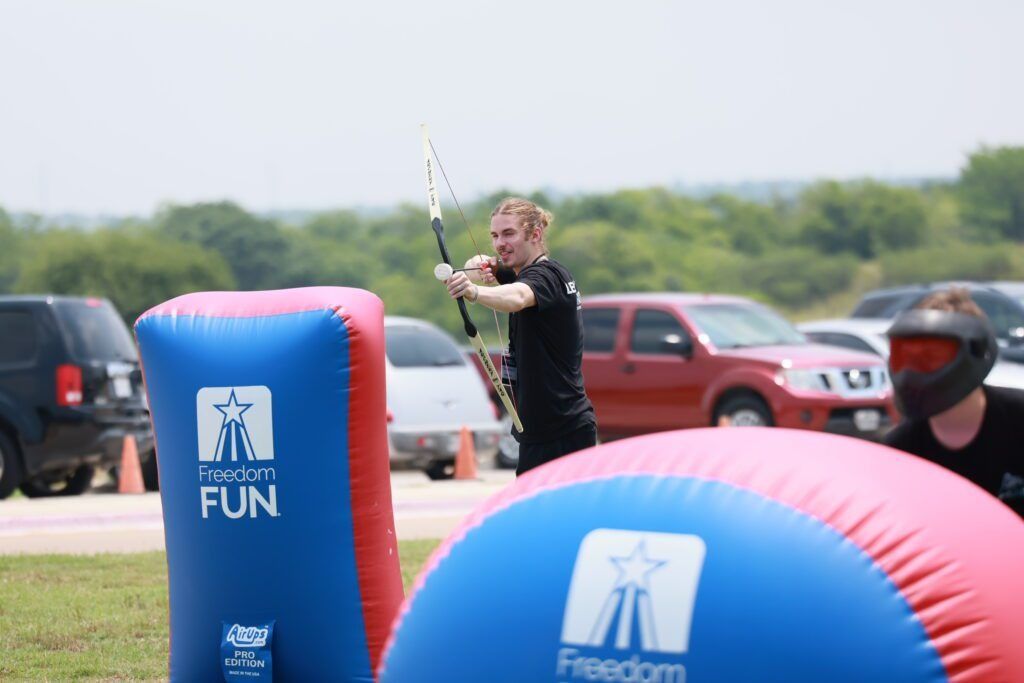 Person aiming a bow behind colorful inflatable barriers at an outdoor event