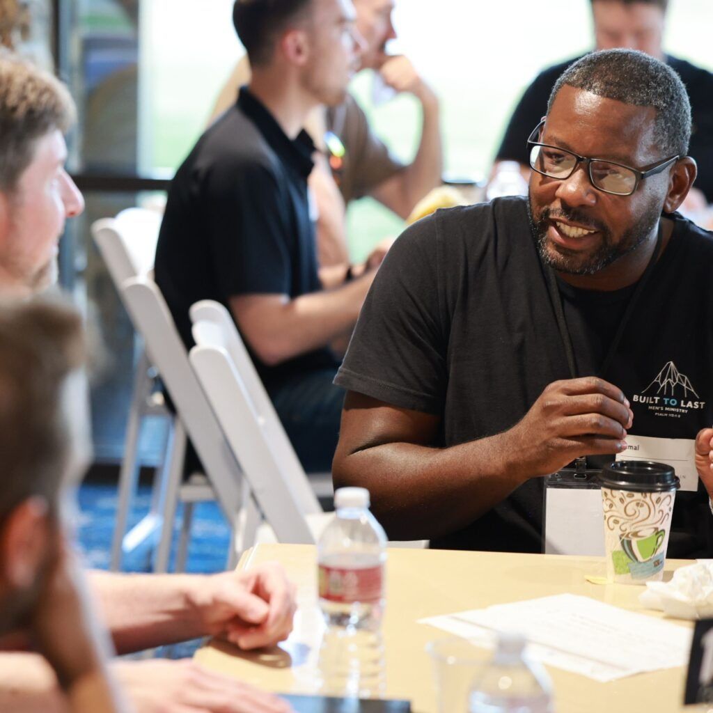 People chatting at a table during a casual indoor gathering, with coffee cups and papers in front of them