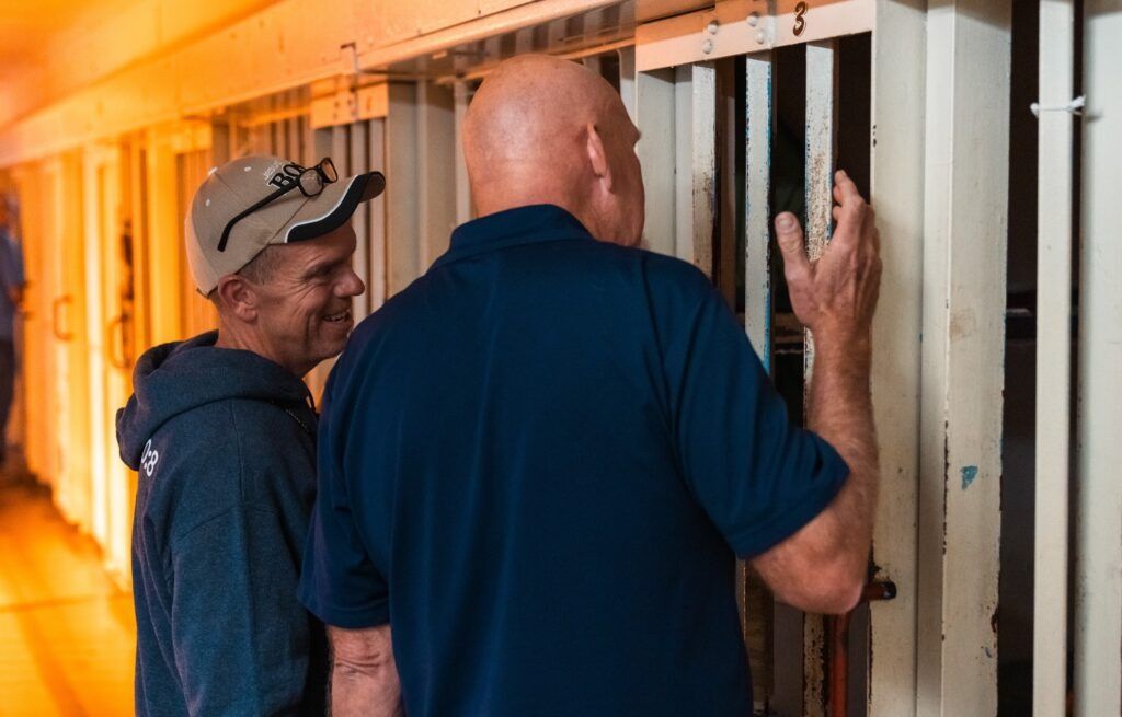 Two men inspect metal bars in a warm-lit industrial corridor