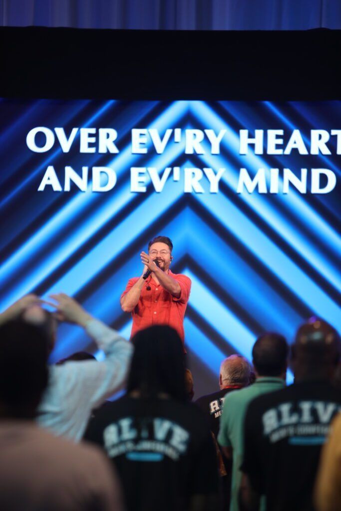 Singer on stage under blue lights with crowd raised hands and text “OVER EVERY HEART AND EVERY MIND”