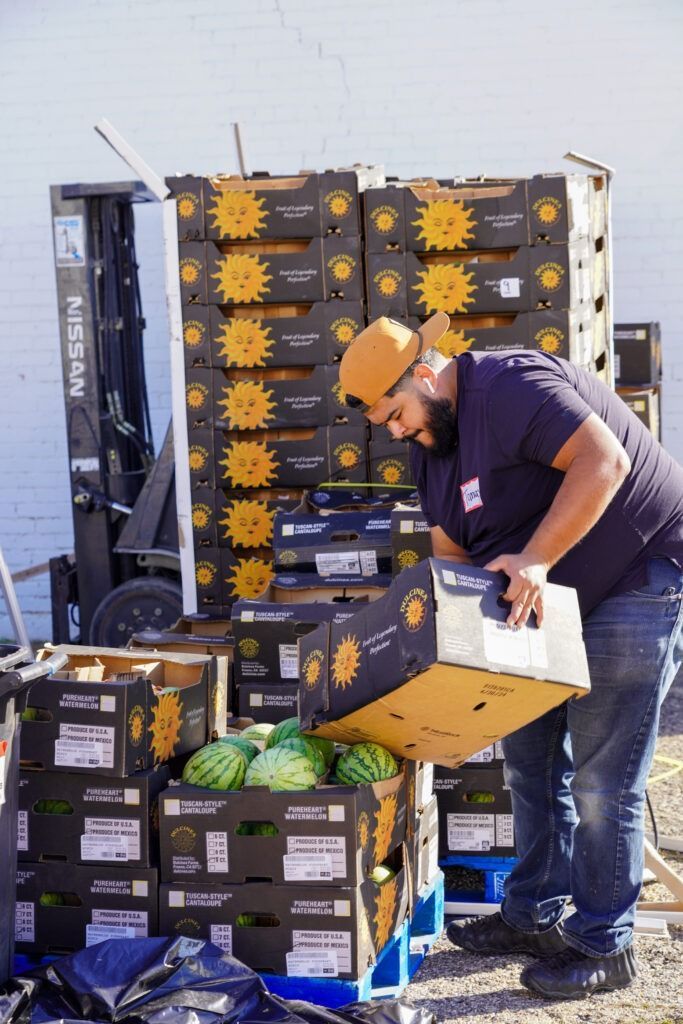 Worker loading stacked produce boxes onto a hand truck at an outdoor market