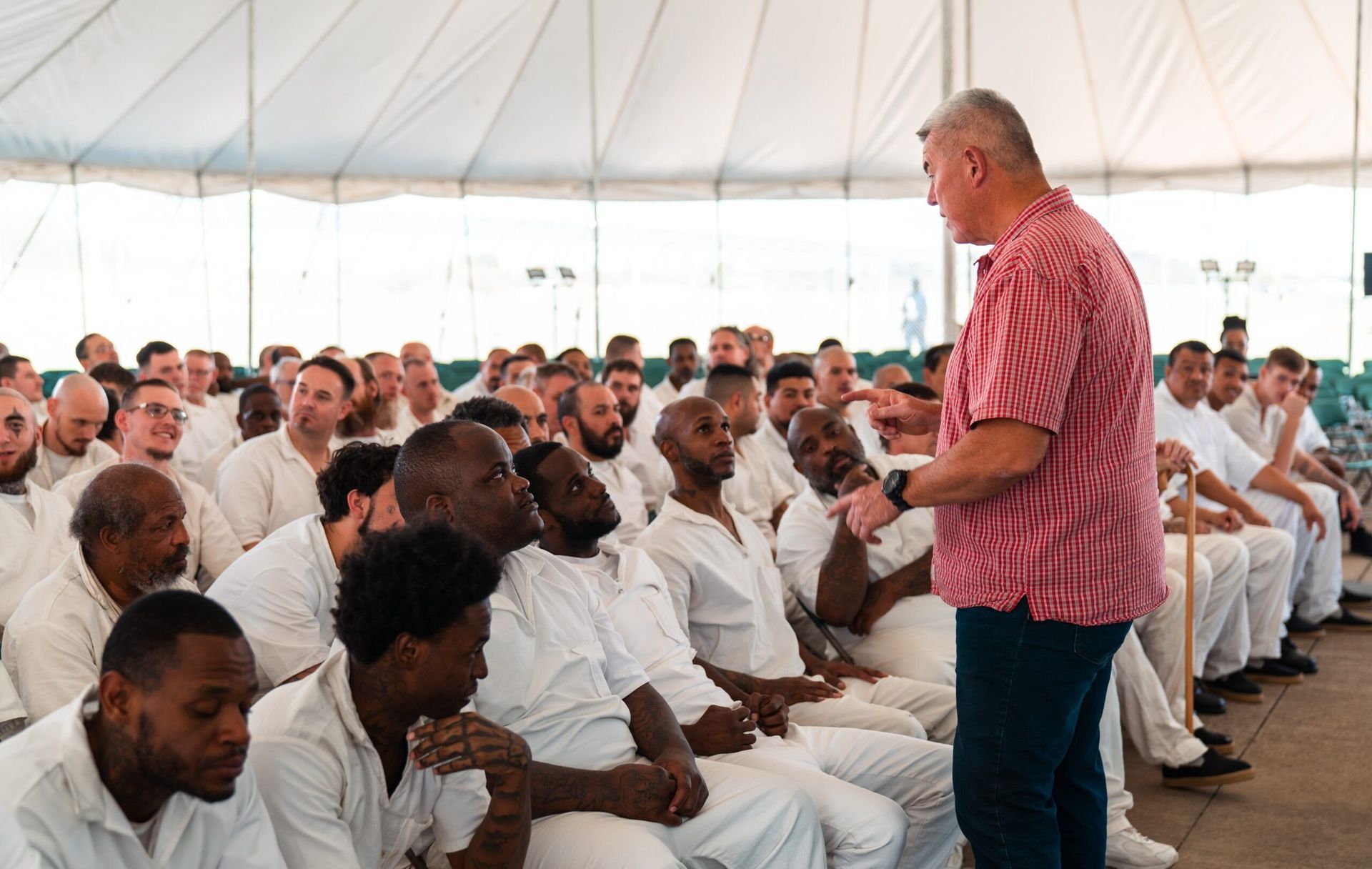 Speaker addressing seated audience in a white tent during a large meeting