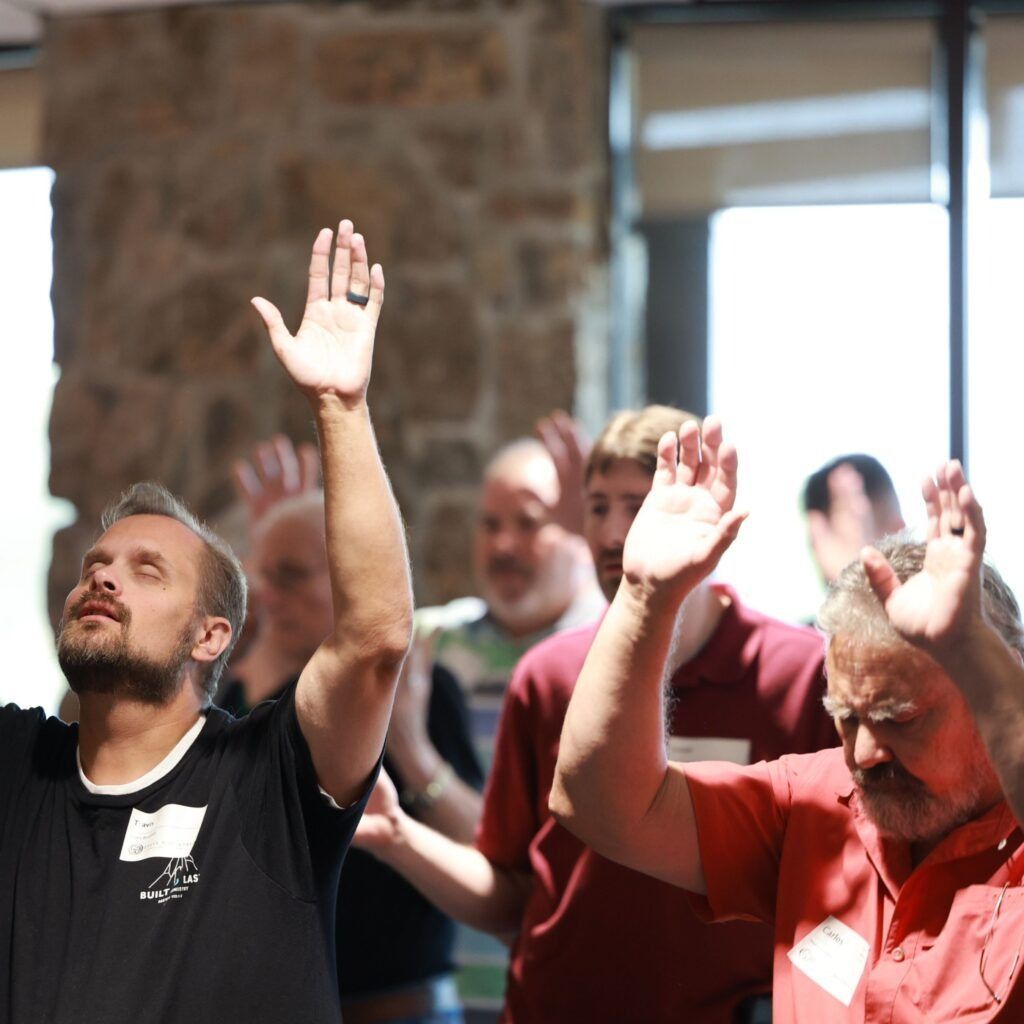 Audience members raising hands during a group event in a sunlit indoor room