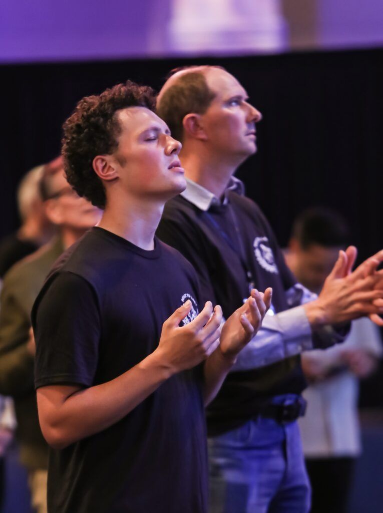 Two people standing with hands raised in a purple-lit indoor gathering