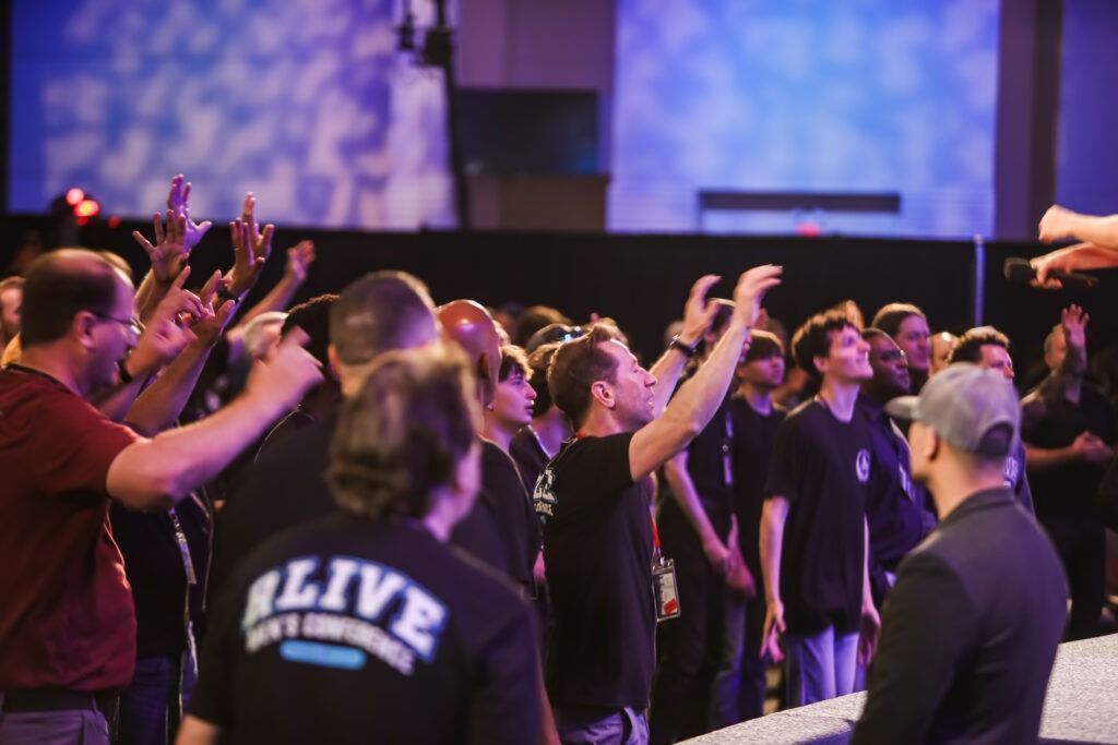 People standing and raising hands in a church worship service with purple stage lighting
