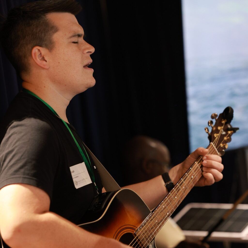Man playing acoustic guitar and singing onstage under warm light