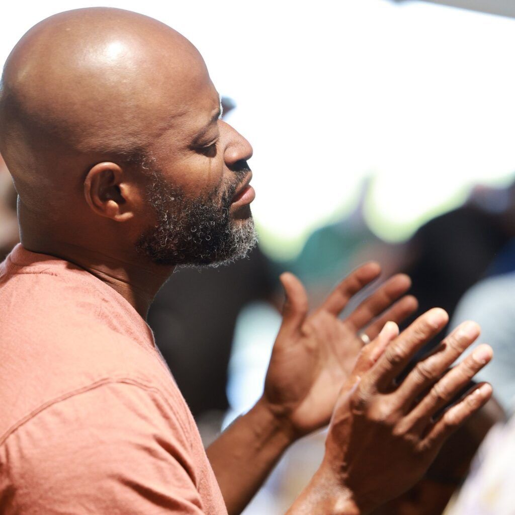 Man clapping outdoors in a peach shirt, shown in profile against a bright blurred background