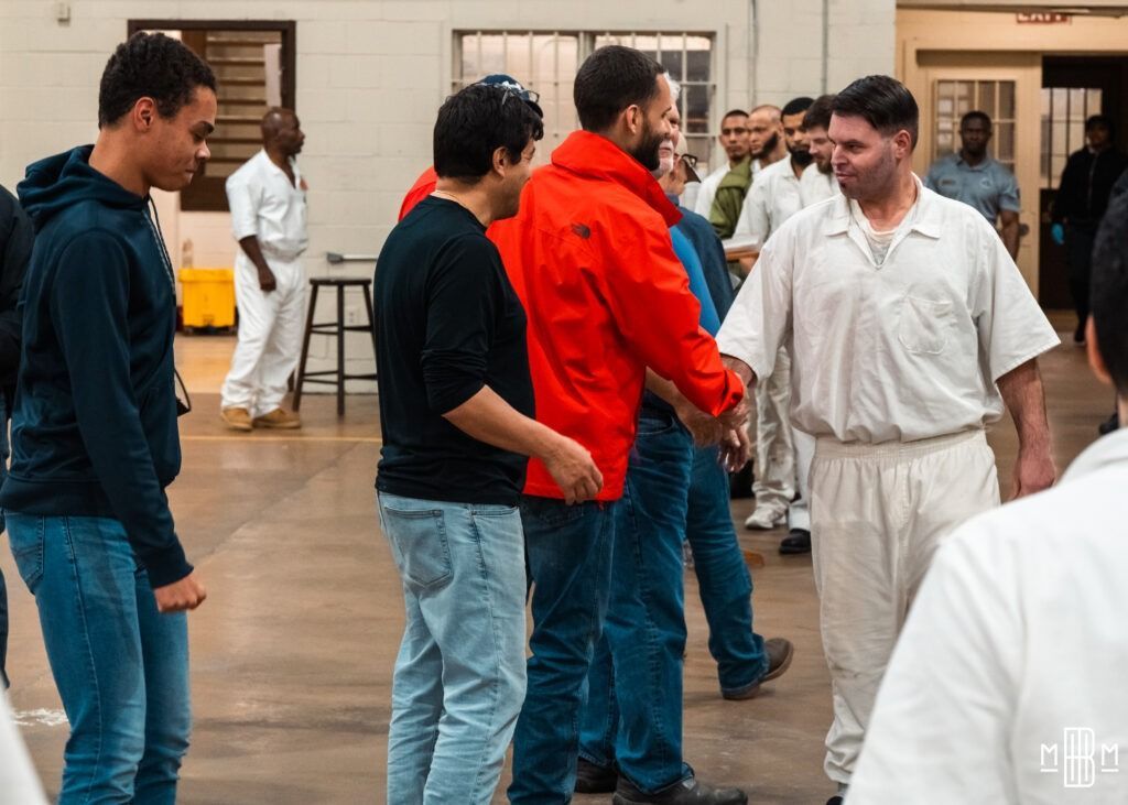 People practicing partner drills in a studio, with one man in a bright red top greeting another in white.