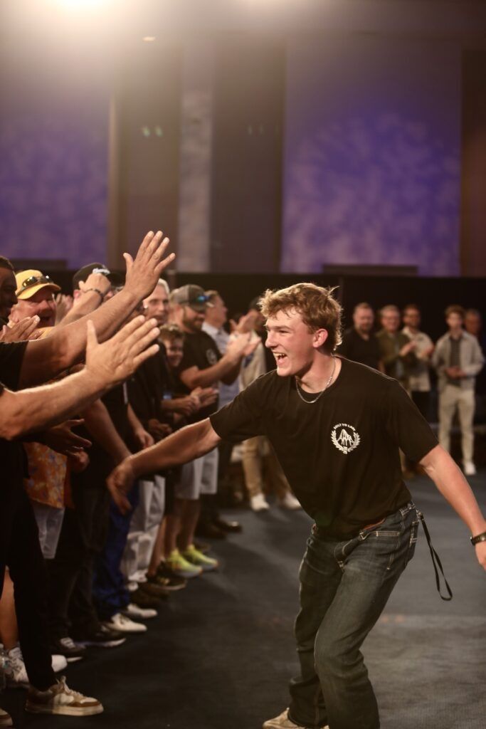 Person high-fiving a crowd at an indoor event, smiling and leaning forward under stage lights