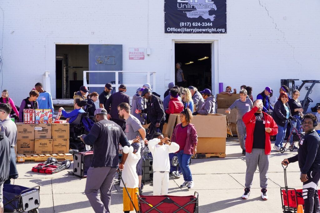 People sorting donated items outside a building, with boxes, clothing, and bags spread across the lot.