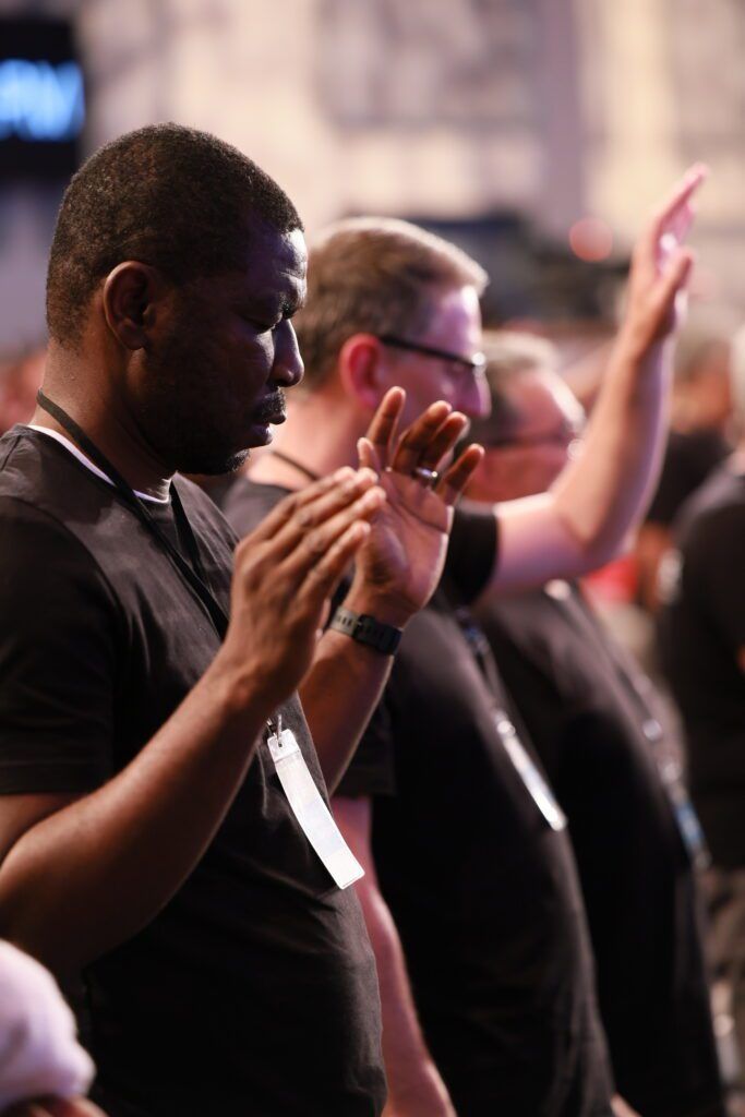People applauding in a dimly lit audience, with one person in the foreground clapping.