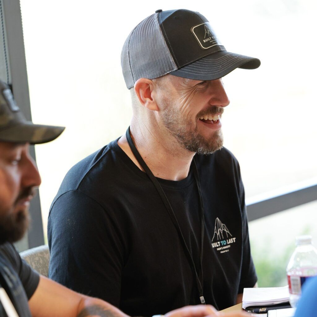 Man in black shirt and gray cap smiling at an indoor event table